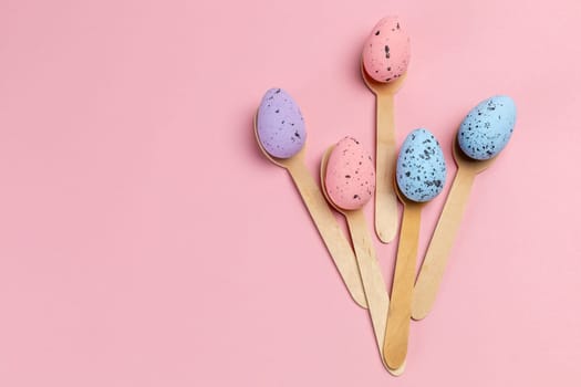 Colored Easter eggs with the wooden spoons on the pink background. Top view.