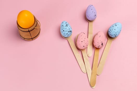 Colored Easter eggs with the wooden spoons and utensil on the pink background. Top view.