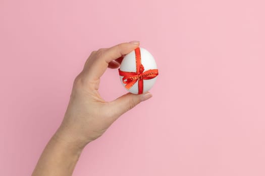 Woman is holding the Easter egg tied with a red ribbon on the pink background. Top view.