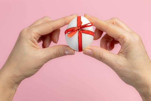 Woman is holding the Easter egg tied with a red ribbon on the pink background. Top view.