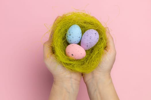 Woman is holding a nest with the Easter eggs. Top view. Pink background.