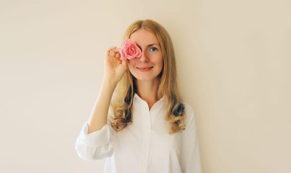 Summer portrait of caucasian happy smiling young woman covering her eyes with pink rose flower buds on studio background