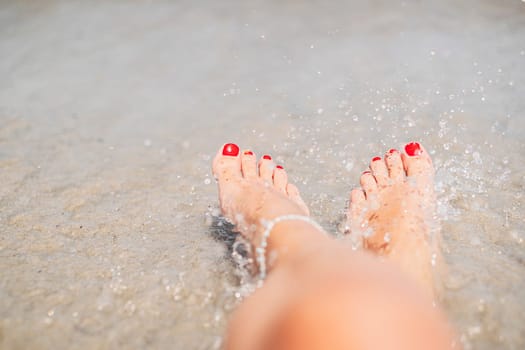 Vacation holidays. Woman feet closeup with red painted nails of girl relaxing on beach on sunny summer day.