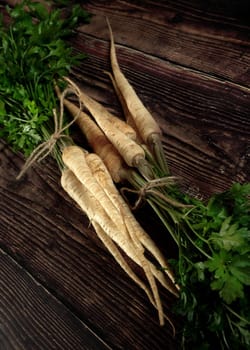 Bunch of parsnip roots and green leaves on dark wooden board
