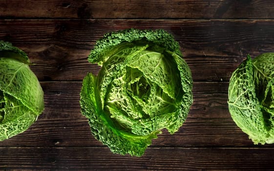 Green savoy cabbage lettuce heads on dark wooden board, view from above