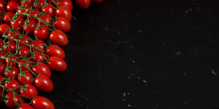 Red cherry tomatoes on black marble like board, wide banner with space for text right side