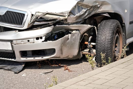 Crashed silver car wreck, detail on front bumper deformed metal plates and tire