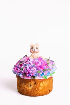 The image shows a small round cake with pink and purple flowers and a bunny on top isolated on a white background.