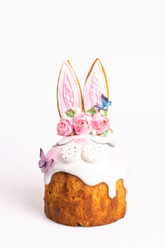 A round cake is decorated with pink frosting and topped with a pair of rabbit ears, roses, and butterflies. Isolated on a white background.