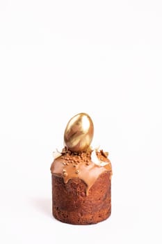 Chocolate cake with creamy icing, topped with gold foil egg on white background. Studio lighting capture.