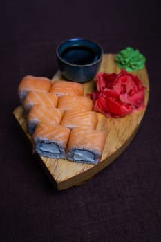 Closeup of traditional Japanese sushi rolls, wasabi paste, and pickled ginger on a wooden plate over dark background