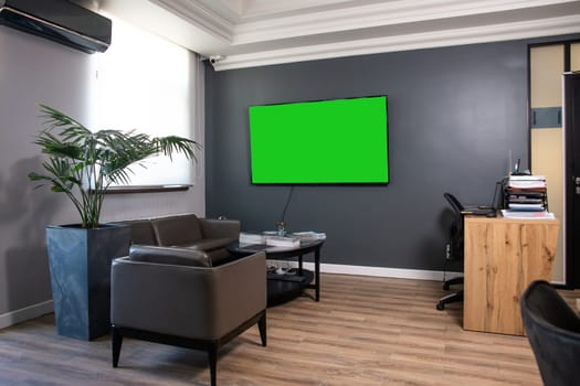 A modern and inviting reception area featuring a vibrant green living wall, sleek large screen TV, and plush seating for guests.