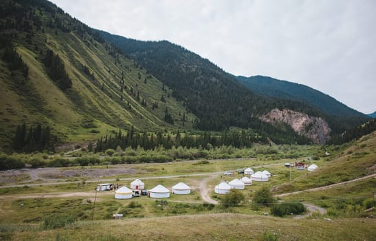 Kyrgyz yurt camp in the mountains of Central Asia. Nomadic village in the valley near the river under cloudy sky.