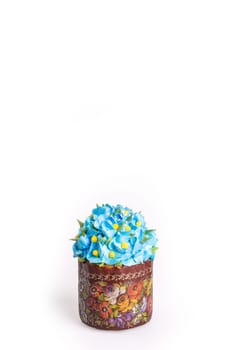 A small round cake with blue icing and delicate flower decorations on a white surface, featuring a golden brown base.