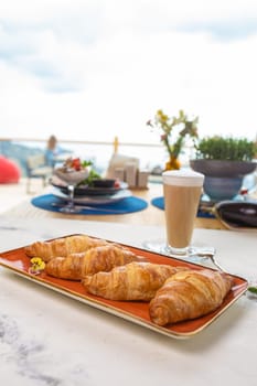 Savor a delectable breakfast spread featuring freshly baked croissants, steaming hot coffee, and a panoramic view from a charming terrace.