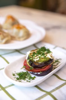 Assortment of grilled vegetables (tomatoes, eggplant, zucchini) stacked with herbs and spices on white background.