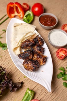 liver kebab with pita bread on a white plate with vegetables and herbs.