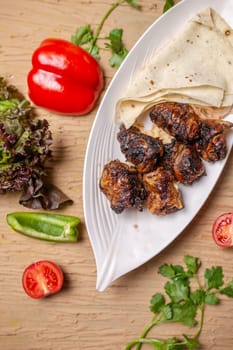 liver kebab with pita bread on a white plate with vegetables and herbs.