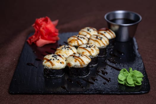 Japanese cuisine, rolls with cheese and sesame seeds and soy sauce on a black plate.