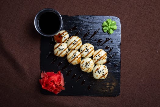 Japanese cuisine, rolls with cheese and sesame seeds and soy sauce on a black plate.