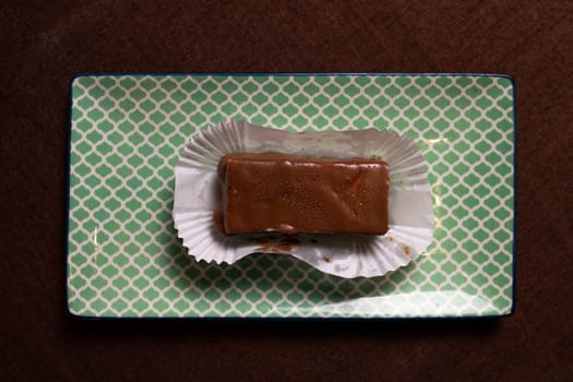 This image shows a piece of homemade chocolate fudge resting on a white paper wrapper on a light green textured background.