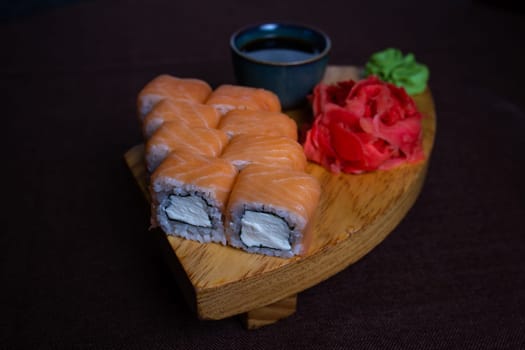 Closeup of traditional Japanese sushi rolls, wasabi paste, and pickled ginger on a wooden plate over dark background