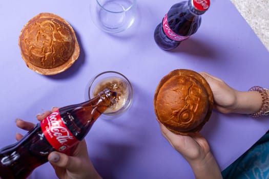 Top view of a hand with burgers and Coca-Cola on a purple table.