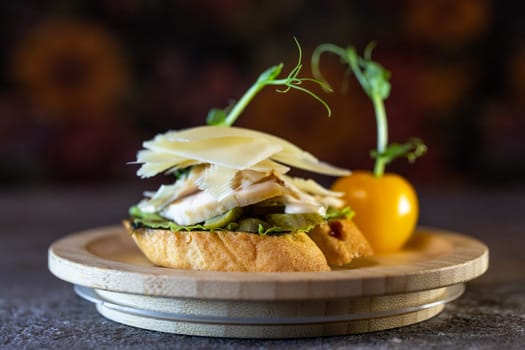 A bruschetta with chicken, pesto, and parmesan. The bruschetta is garnished with microgreens and a pea pod.