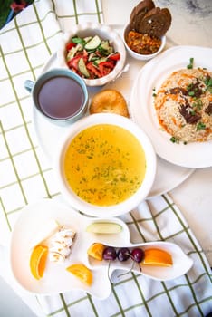 Uzbek national dishes, plov, shurpa, salad, and non on a tray with tea. Traditional Uzbek food. Checkered tablecloth background.