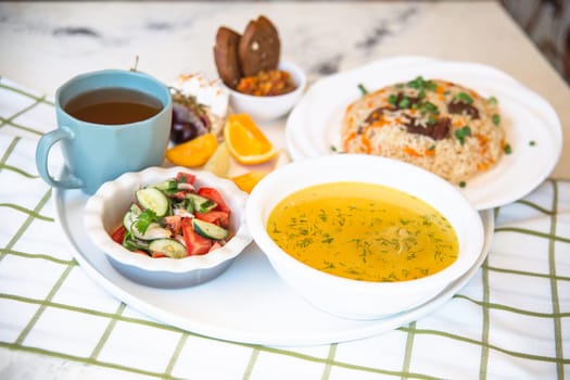 Uzbek national dishes, plov, shurpa, salad, and non on a tray with tea. Traditional Uzbek food. Checkered tablecloth background.