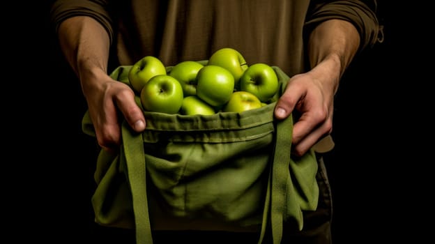 A man holds in his hands a large number of green apples in a bag made of natural fabric. The concept of recycling, saving, fighting plastic, proper nutrition, healthy lifestyle, diet, veganism, vegetarianism, gardening and farming, fresh fruit