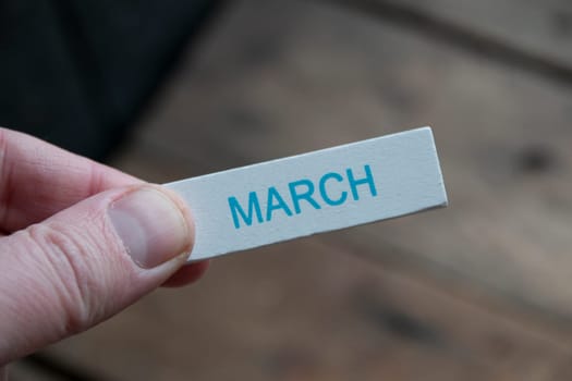 Hello March creative concept. A hand holds a sign with an inscription.