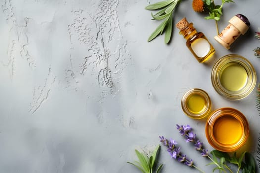 Four glass jars with aromatic oils, medicinal flowers and rosemary branches lie on the right on a gray background with copy space on the left, flat lay close-up.