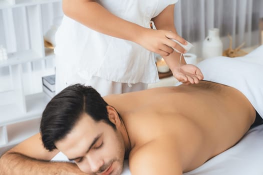 Caucasian man customer enjoying relaxing anti-stress spa massage and pampering with beauty skin recreation leisure in day light ambient salon spa at luxury resort or hotel. Quiescent