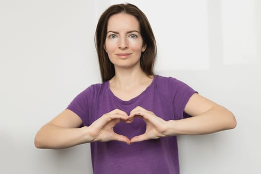 Inspire inclusion. Woman holding her hands in the shape of a heart and holding them in front of her, dressed purple t-shirt. International women's day concept