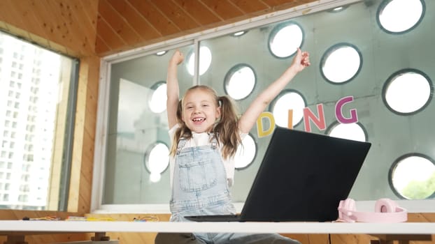 Happy girl looking at camera while raised hands to celebrate success project. Smart cute student finish writing, programing system and shouting with happiness in STEM technology class work. Erudition.