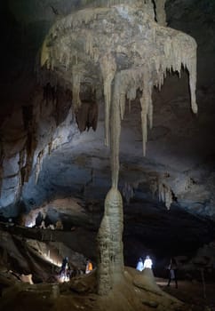 Tourists with headlamps explore a cave, illuminating stunning stalactite and stalagmite formations.