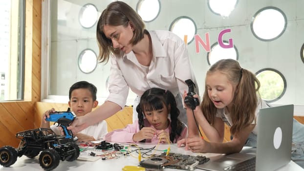 Teacher looking at children while diverse student looking at screen. Children excited in presentation while drawing or writing art books at table with toys and color pencil placed on table. Erudition.