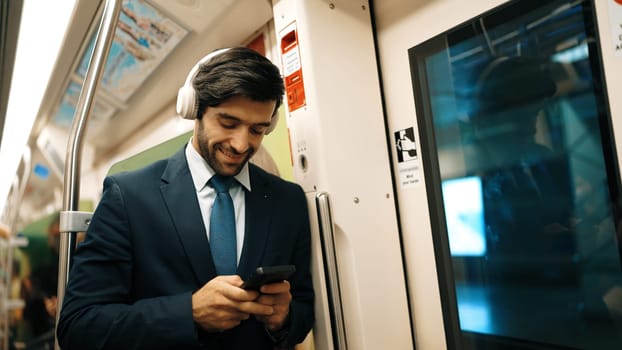 Smart executive manager wear headphone and listen music while standing in train. Professional business man lean at partition while listen relaxed song and choosing songs. Business concept. Exultant.