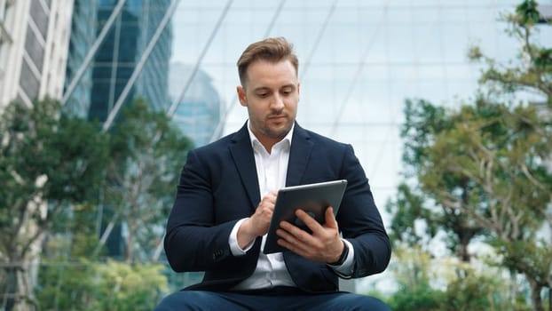 Close up of businessman sitting at park while writing on tablet by using tablet pencil and planning marketing strategy. Manager looking at data analysis while thinking about financial plan. Urbane