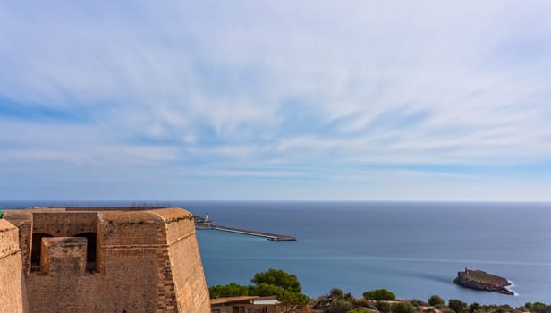 Long exposure photo of Dalt Vila castle in Ibiza, featuring the harbor, sea, and visible tourist trails over the castle.