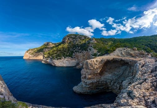 Picturesque cliffs by calm sea with vibrant greenery under a bright blue sky.