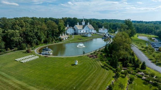 Aerial View Showcasing A Cluster Of Traditional White Orthodox Churches With Cross-Topped Domes, Arranged Around A Curved Pond With A Fountain, Amidst Green Trees And Neatly Arranged White Benches