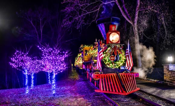 Elizabethtown, Pennsylvania, USA, December 8,2023 - Vibrant Night Scene Of A Festively Decorated Steam Locomotive With Christmas Lights, Wreaths, American Flags, Flanked By Trees With Purple Lights.
