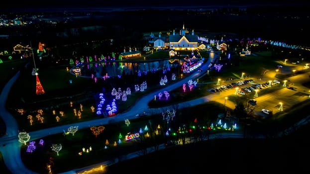 Expansive Aerial View Of A Festive Grounds Illuminated With Holiday Lights Featuring A Path To A Pond And Multiple Buildings At Night.