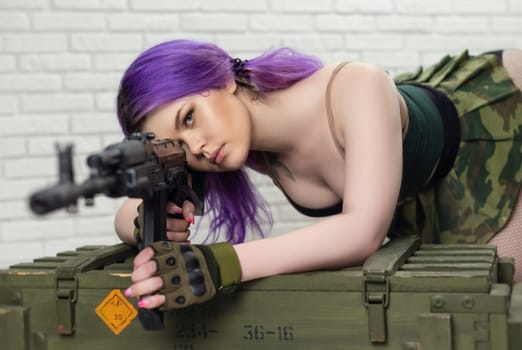 hot girl in a short sexy military skirt with a Kalashnikov assault rifle and a gun case on brick wall background copy paste