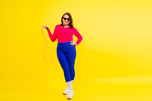 Pretty smiling plump female in a sporty top and leggings holding jumping rope in hands