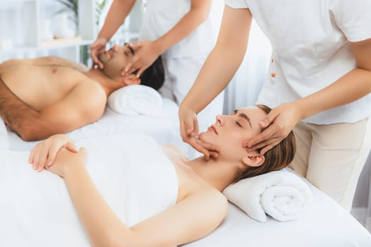 Caucasian couple enjoying relaxing anti-stress head massage and pampering facial beauty skin recreation leisure in dayspa modern light ambient at luxury resort or hotel spa salon. Quiescent