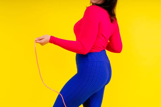 Pretty smiling plump female in a sporty top and leggings holding jumping rope in hands