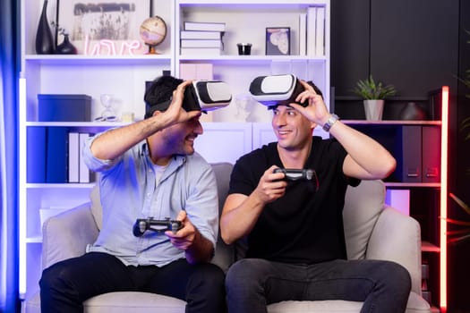 Buddy friend gamers playing video game using joysticks and VR headset of virtual technology in reality in studio room with neon blue light. Comfy living indoor with cheerful fighting winner. Sellable.